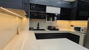 A modern kitchen with a white countertop, black cabinets, a gas stove, a microwave, and a window above the sink.