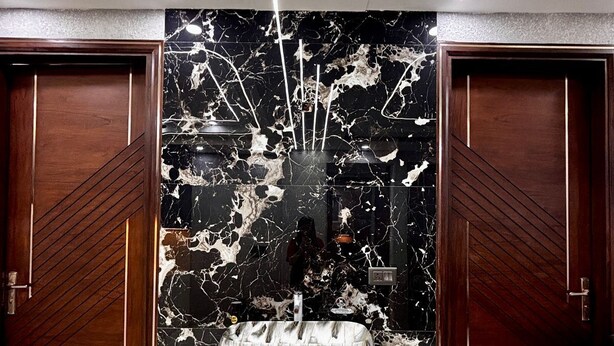 A modern bathroom with a marble vanity, a black and white marble backsplash, and wooden doors.