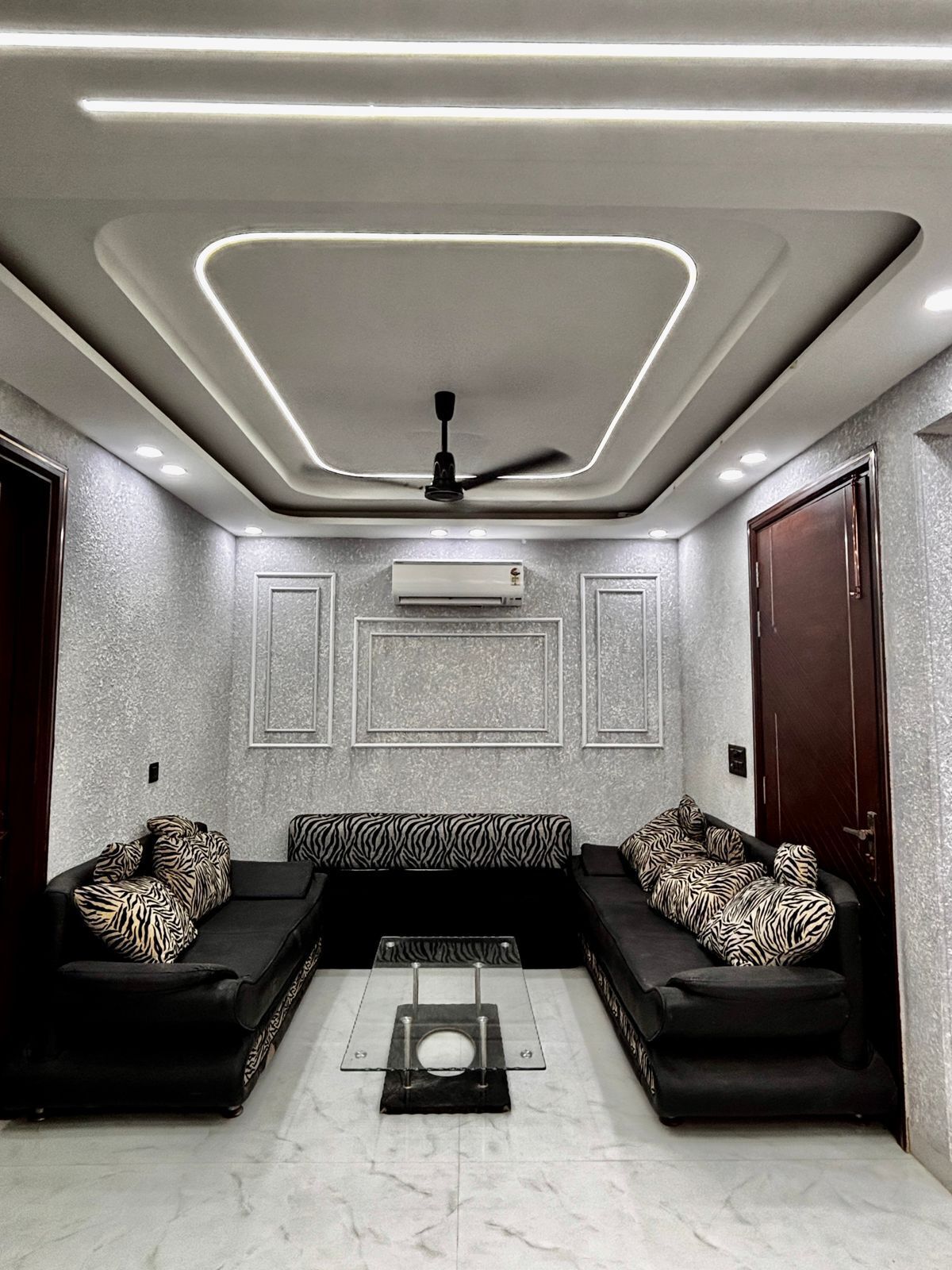 A modern living room with a sectional sofa, a ceiling fan, recessed lighting, and a marble floor.