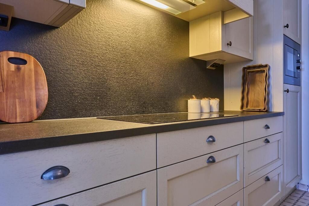 Een keuken met witte kastjes, een zwart aanrecht en een houten snijplank.