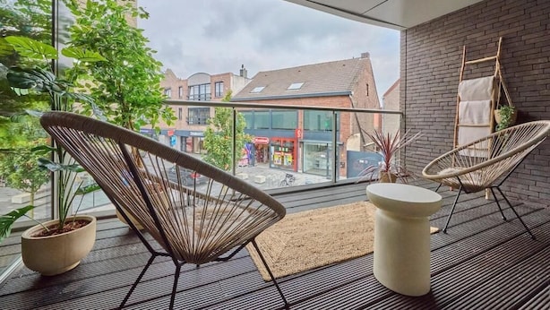 Une pièce moderne avec de grandes fenêtres, des chaises en osier, une plante en pot et une petite table.