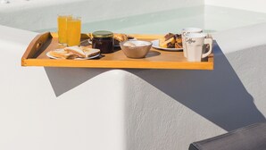 Bandeja de desayuno con tostadas, jugo, café y pastelería en un balcón con piscina y un cojín verde.