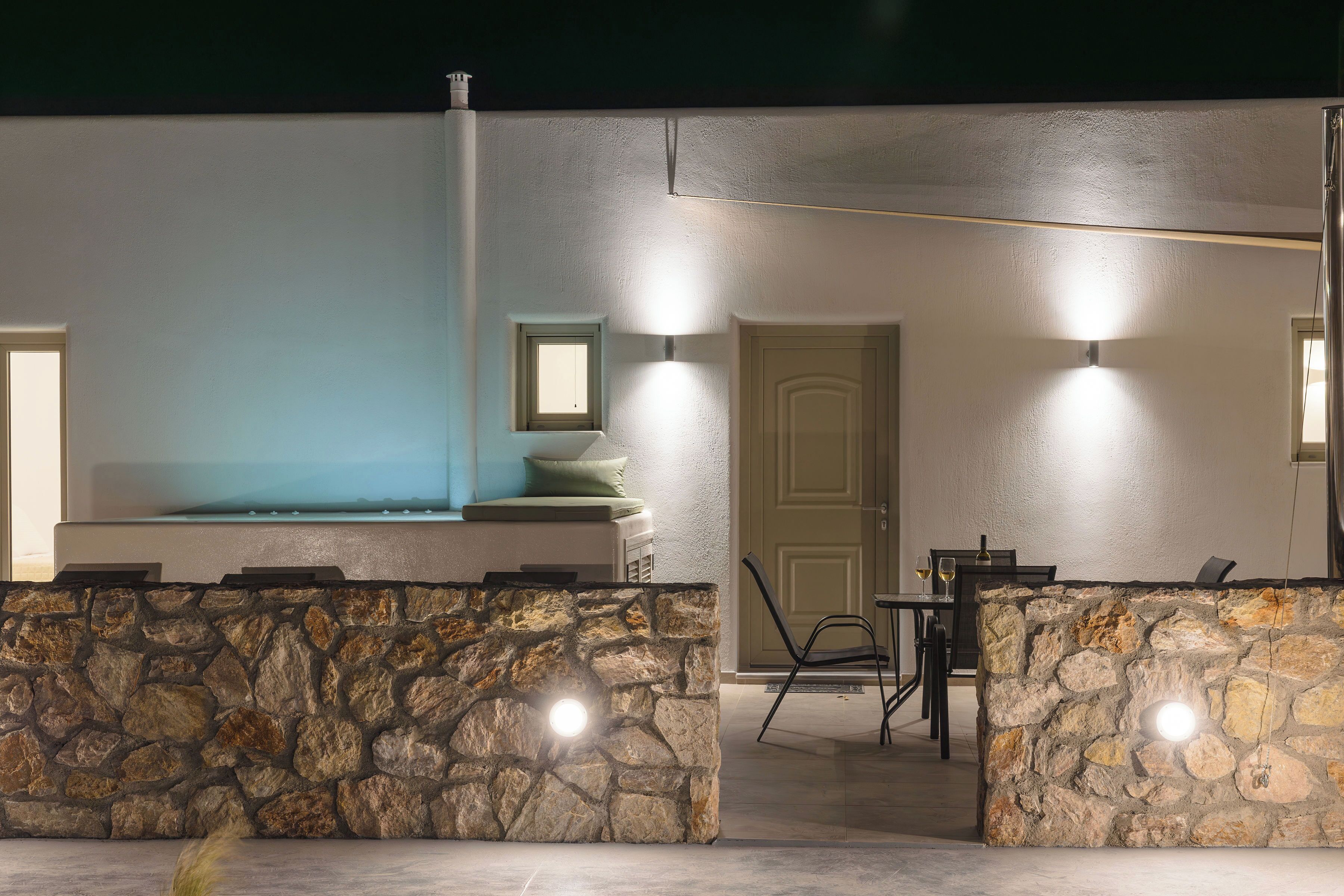 A stone wall with a built-in seating area, a pool, and a dining setup with chairs and a table.