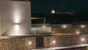 Un espacio exterior moderno con un muro de piedra, un cerramiento de vidrio y un molino de viento al fondo.
