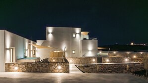 Un edificio moderno con fachada de piedra, piscina y una entrada bien iluminada.