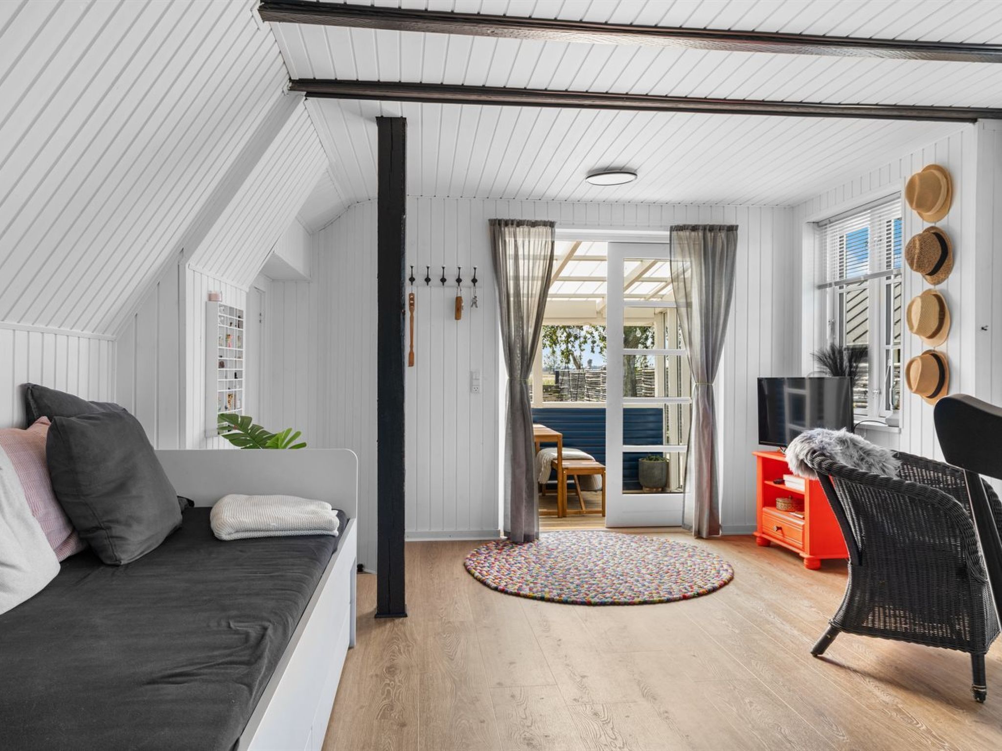 A cozy loft-style room with a bed, a sofa, a wicker chair, and a TV.