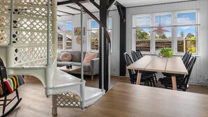 A spacious room with a dining table, chairs, a sofa, and a white staircase with intricate lattice design.