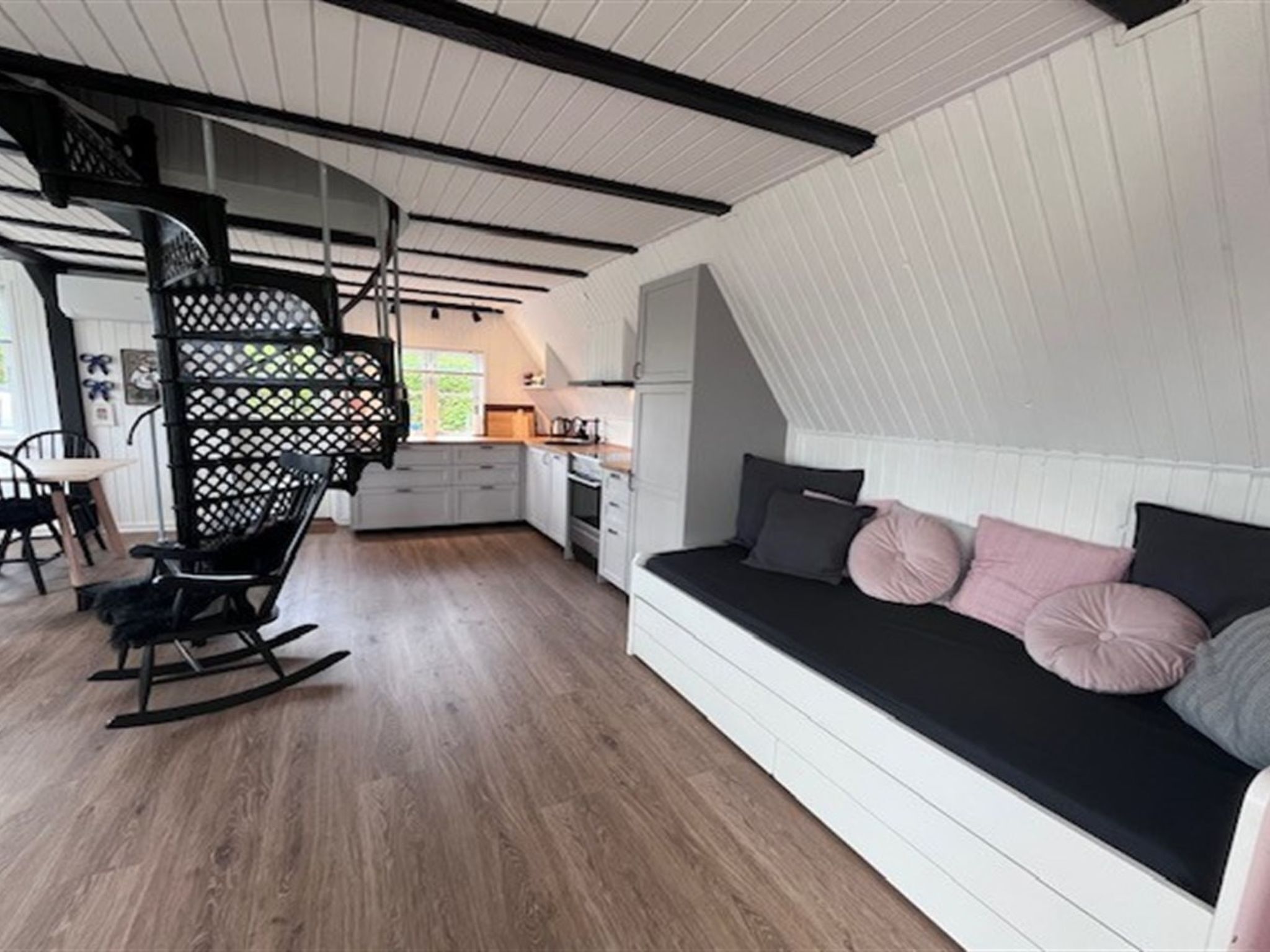 Une chambre de style « loft », avec un canapé noir, un plancher en bois et un escalier en colimaçon.