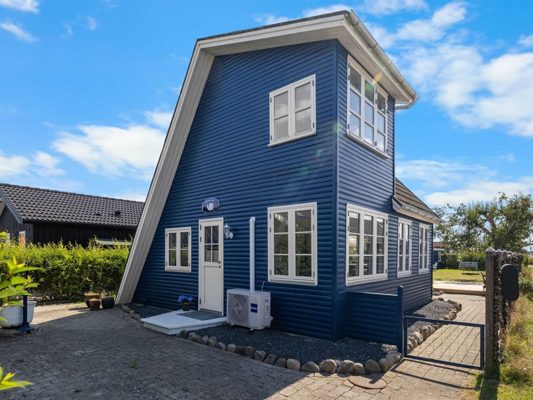 A two-story blue house with white trim, a front porch, and a small air conditioning unit.