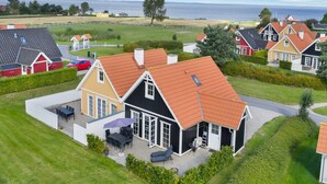 Een woonwijk met huizen met rode dakpannen, een terras met tuinmeubels en uitzicht op de zee.