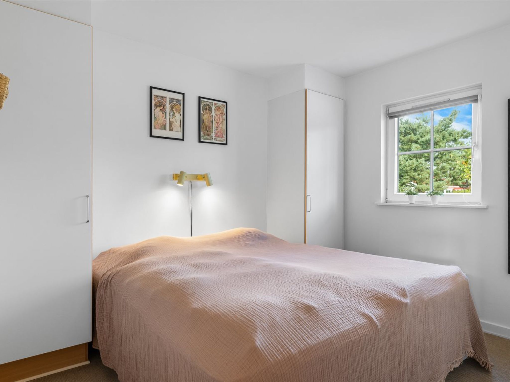 A bedroom with a bed, a window with a view, and two framed pictures on the wall.