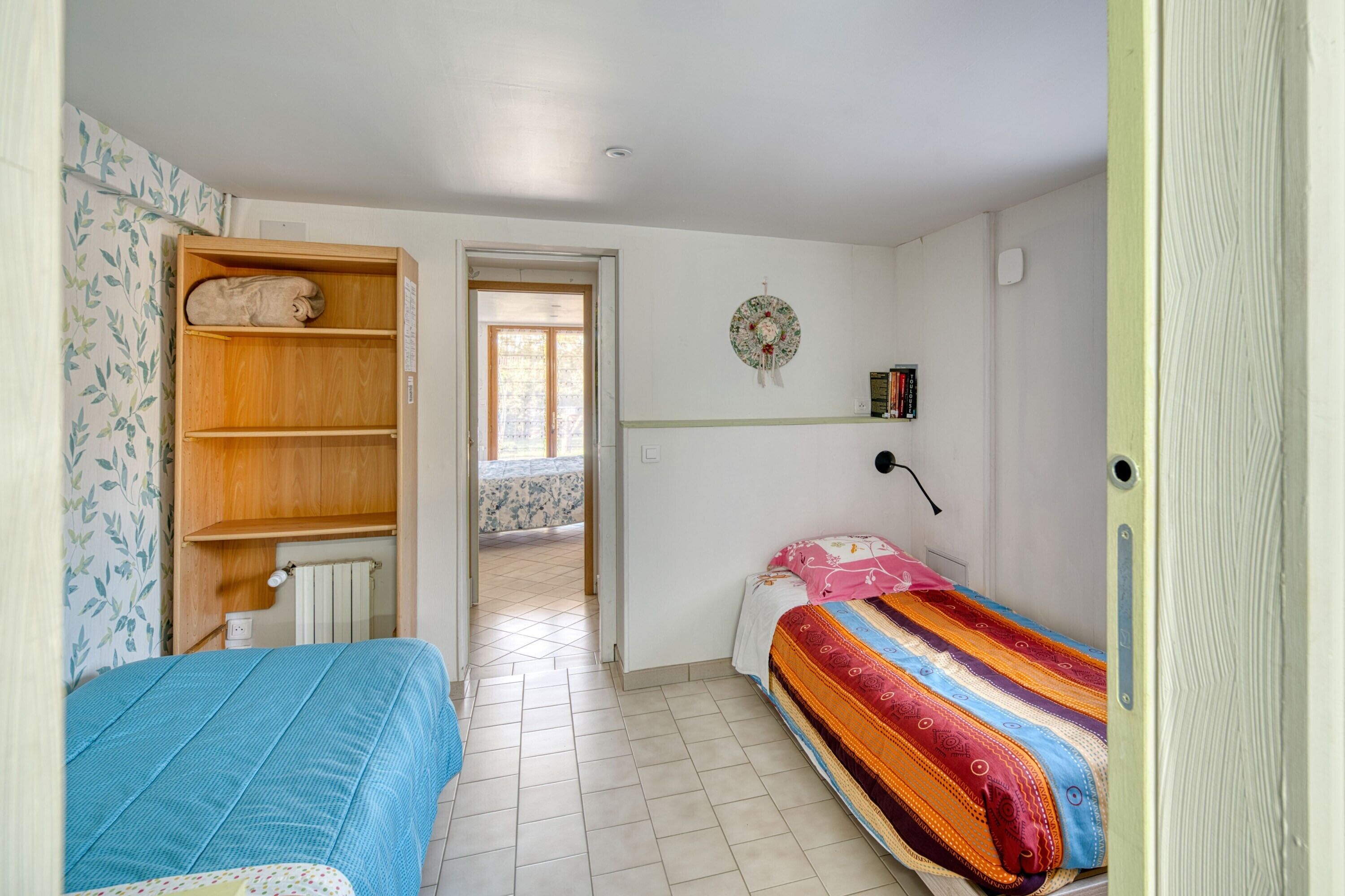 Ein Schlafzimmer mit zwei Betten, einem Holzschrank, einer Wandablage und einer Tür zu einem anderen Raum.