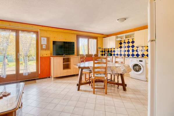 A kitchen with a dining table, chairs, a washing machine, and a television.
