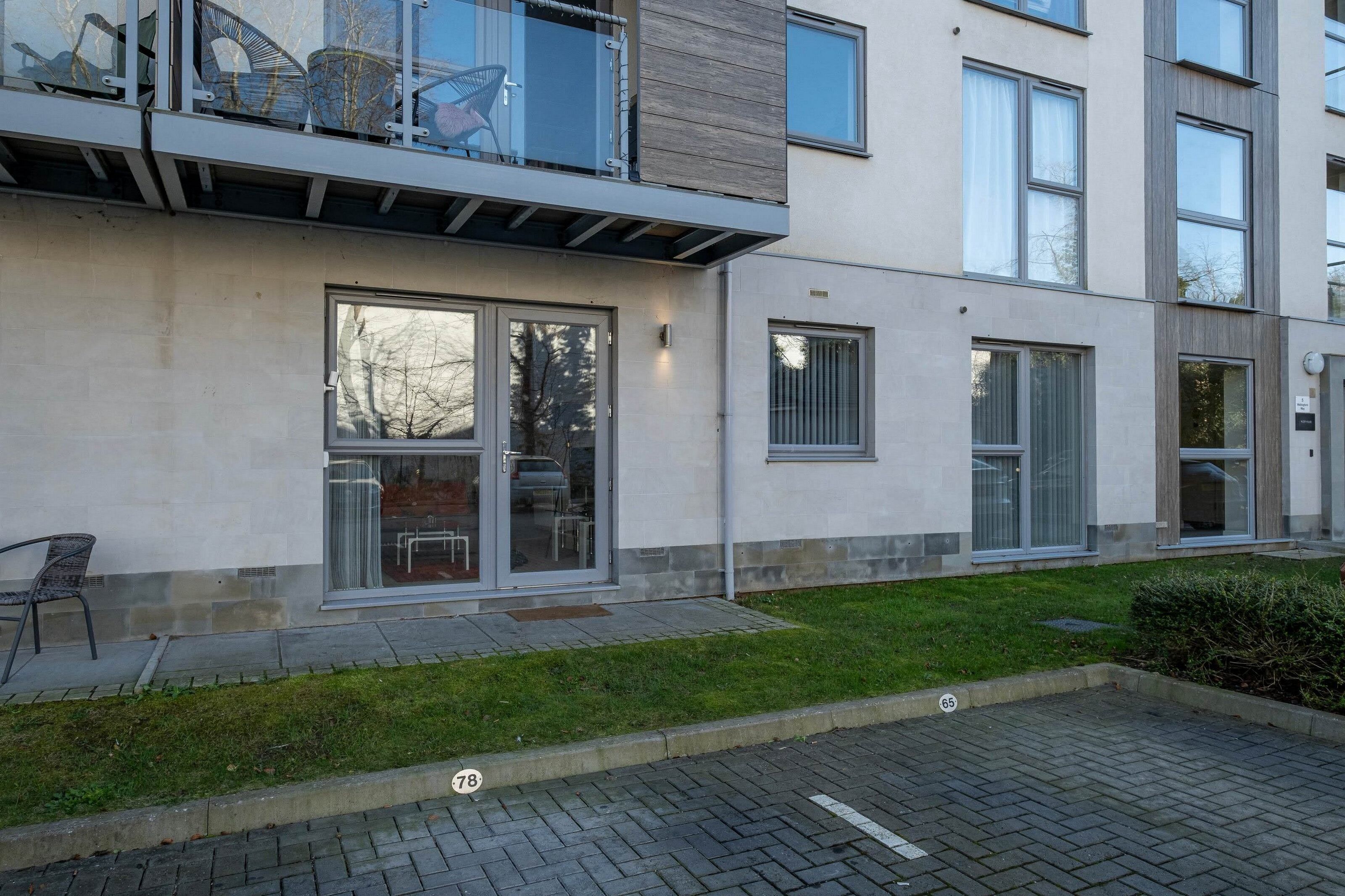 Un moderno edificio de apartamentos con balcón de cristal, ventanas amplias y una entrada empavedada.
