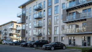 Egy többemeletes lakóépület, amelynek erkélyei vannak, egy parkoló, ahol több autó is található, és tiszta az ég.