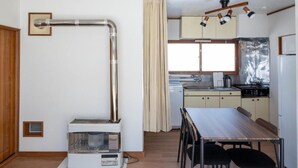 A compact kitchen with a stove, sink, and cabinets. There is a dining table with chairs and a small heater on the floor. - FURANO RELAX STAY BC (Furano)