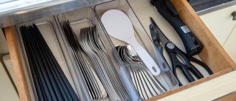 A drawer containing various kitchen utensils including forks, knives, and a brush.