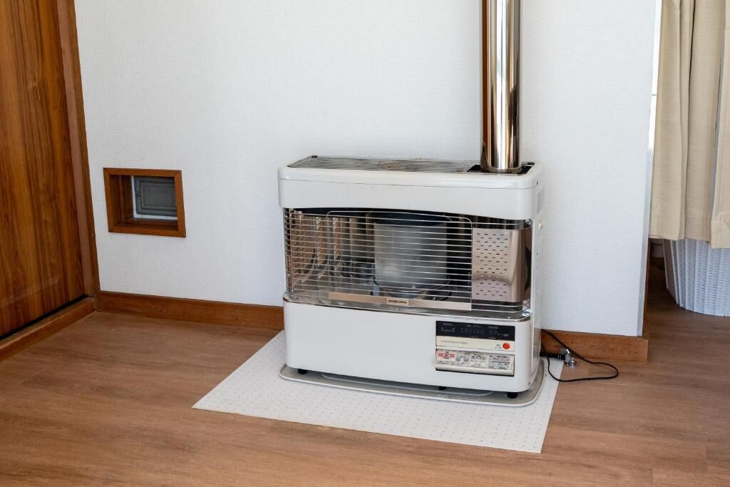 A portable heater with a control panel, placed on a mat in a room with wooden flooring and a white wall.