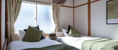 A hotel room with two beds, a window with curtains, a hanging lamp, and a framed picture on the wall.