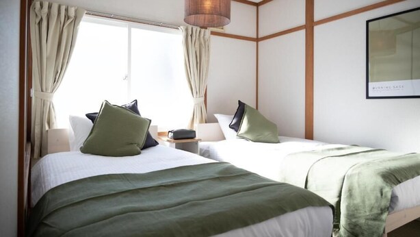 A hotel room with two beds, a large window with curtains, a hanging lamp, and a framed picture on the wall. - FURANO RELAX STAY BC (Furano)