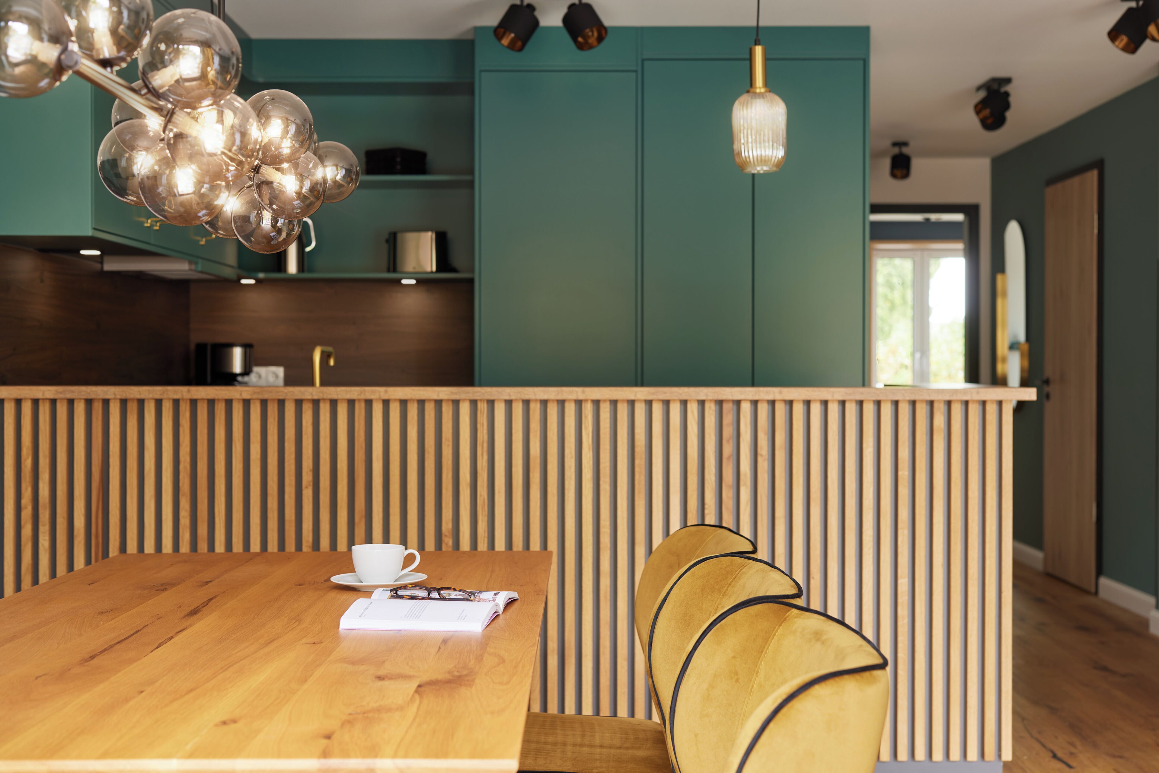 A modern kitchen with teal cabinets, a wooden island, and a dining area with a wooden table and chairs.
