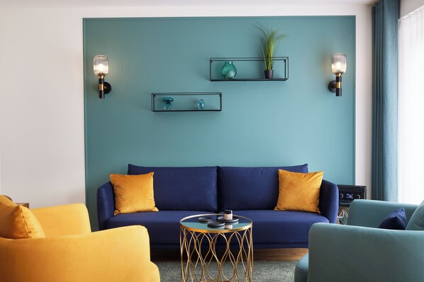 A modern living room with a teal accent wall, a blue sofa with yellow cushions, and a round coffee table. - Completion 2025: Very modern apartment with sauna and two bedrooms! (Sankt Peter-Ording)