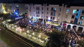 Un gran grupo de personas reunidas al aire libre frente a un edificio con varios balcones y un corredor cubierto.