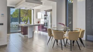 Een moderne keuken met een centraal eiland, een eethoek met een glazen tafel en stoelen, en uitzicht op de omgeving.