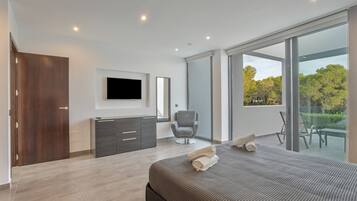 Un dormitorio moderno con una cama, un televisor, una silla y un ventanal corredera a un balcón.