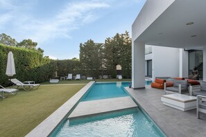A modern outdoor pool area with a rectangular pool, lounge chairs, and a seating area with cushions.