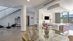 Een ruime woonkamer met een glazen eettafel, zithoek en een moderne keuken, plus een trap.