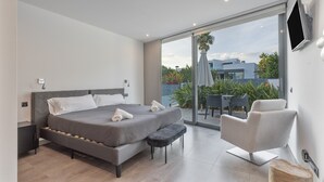 Een moderne slaapkamer met een groot bed, een bankje, een televisie en een balkon met tuinmeubilair.