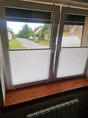 Ein Zimmer mit Fenster zur Straße, darunter eine Heizung und ein Holzregal.