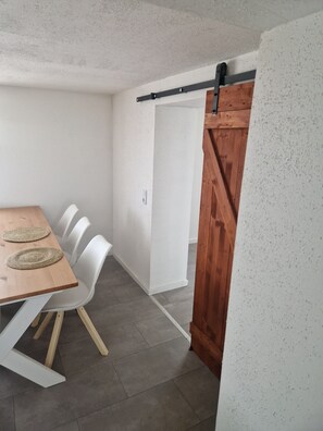 Ein Essbereich mit Holztisch, weißen Stühlen, einer Schiebetür im Bauernhausstil und einer weißen Wand.