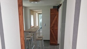 A hallway with a wooden door, a table with stools, and a tiled floor.