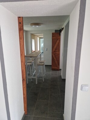 A hallway with a wooden door, a table with stools, and a tiled floor.