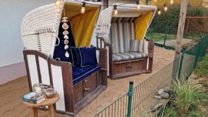 Two wicker sofas with cushions, a small wooden table with books and a candle, and a string of lights.