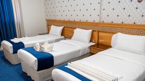 Une chambre d’hôtel avec trois lits simples, chacun recouvert d’une courtepointe bleue et blanche, dotée d’oreillers blancs et d’une tête de lit en bois.