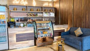 Un café avec un comptoir en bois, des étagères remplies de collations et de boissons, une machine à café et un canapé bleu.