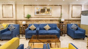Un hall d’entrée avec trois canapés bleus, un fauteuil jaune et une table basse en verre.