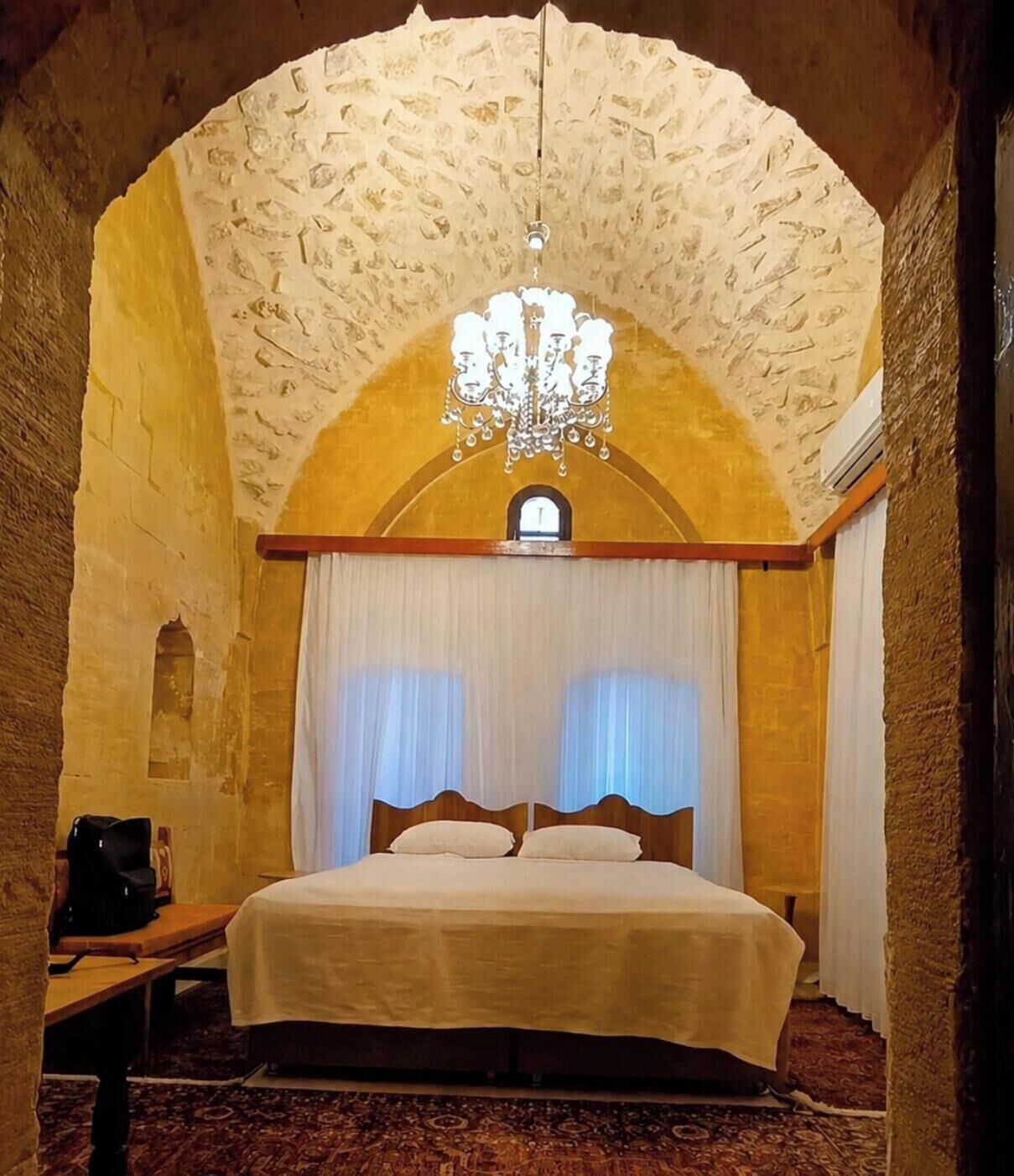 Una habitació amb un llit, una làmpada de cristall i una arcada de pedra.