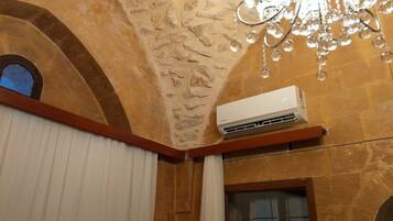 Une pièce avec un mur en pierre, un climatiseur fixé au mur, une fenêtre avec des volets en bois et un lustre.