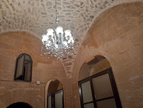 A chandelier hanging from a ceiling with a stone pattern. There are arched doorways and windows. - Yücesoy Konağı (Mardin)