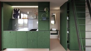 A modern kitchen with green cabinetry, a stainless steel sink, and a built-in stove. There is a small island with a sink and a mirror above it.