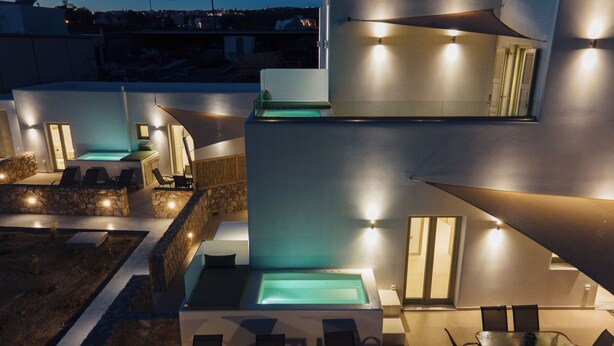 Un espace piscine extérieur moderne, doté de chaises longues et d’une table à manger, entouré de murs en pierre et abrité par une grande avancée de toit.