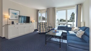 A hotel room with a sofa, armchair, and a glass coffee table. There is a TV on a cabinet, and a window with curtains. - "Apartment am Kurstrand" Vacation Rental in Zingst, Right on the Pier (Zingst)