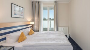 A hotel room with a large bed, two pillows, a bedside table, a lamp, a framed picture on the wall, and a window with curtains. - "Apartment am Kurstrand" Vacation Rental in Zingst, Right on the Pier (Zingst)
