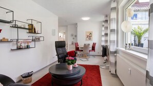 A modern living room with a black leather sofa, a round coffee table with a red rug, and a dining area with a red chair. - Apartment 'Ferienwohnung Steffi' with Private Terrace and Wi-Fi (Laichingen)