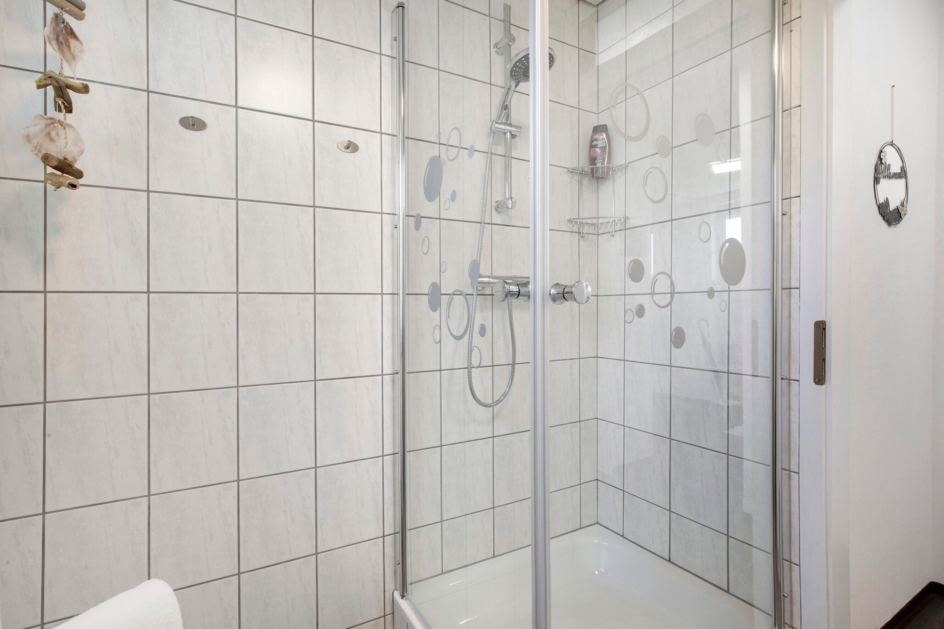 Une douche fermée par des parois de verre, dotée d’un pommeau de douche à main, d’un robinet mural et d’une porte en verre.