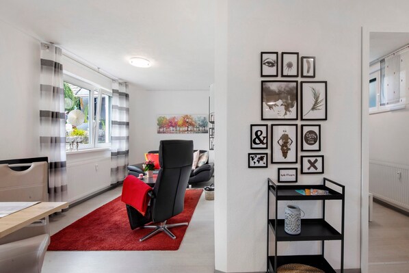 Una sala de estar moderna con un tapete rojo, una silla negra, un sofá blanco y una pared decorada con fotografías enmarcadas.